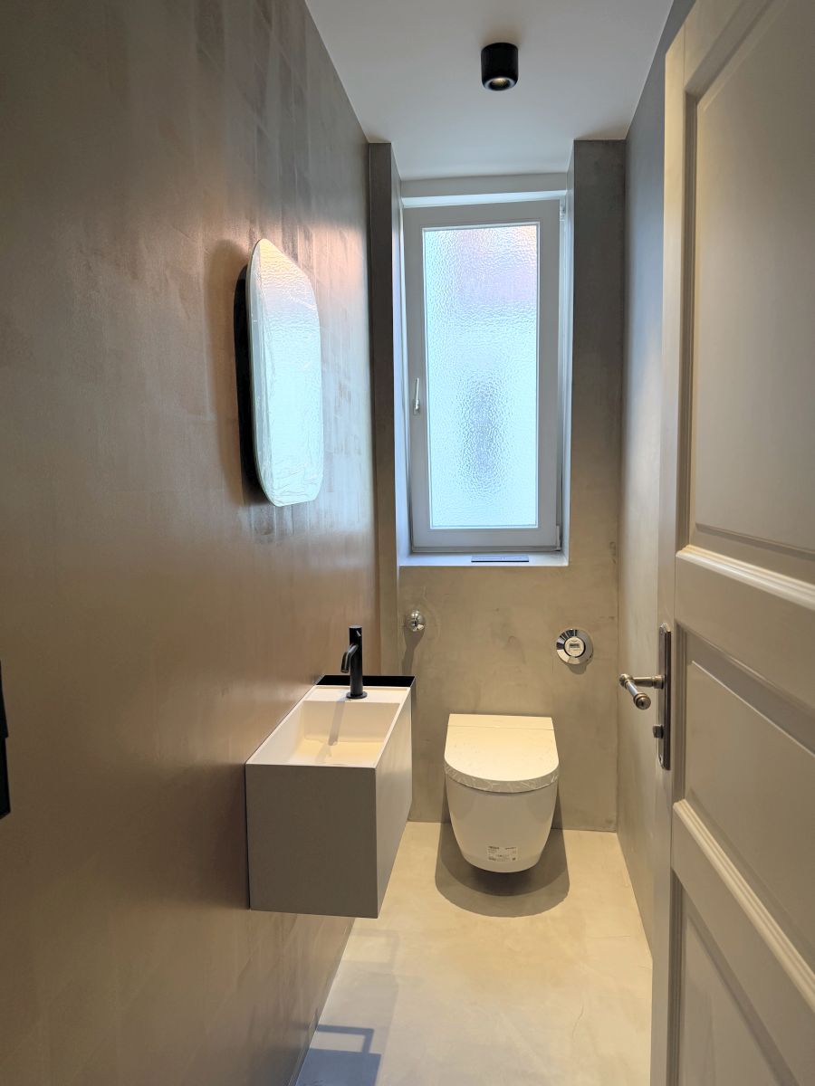 Saniertes Gäste-WC mit fugenlosen Wänden und Boden in Mikrozement, Wand-WC und weißem Waschbecken