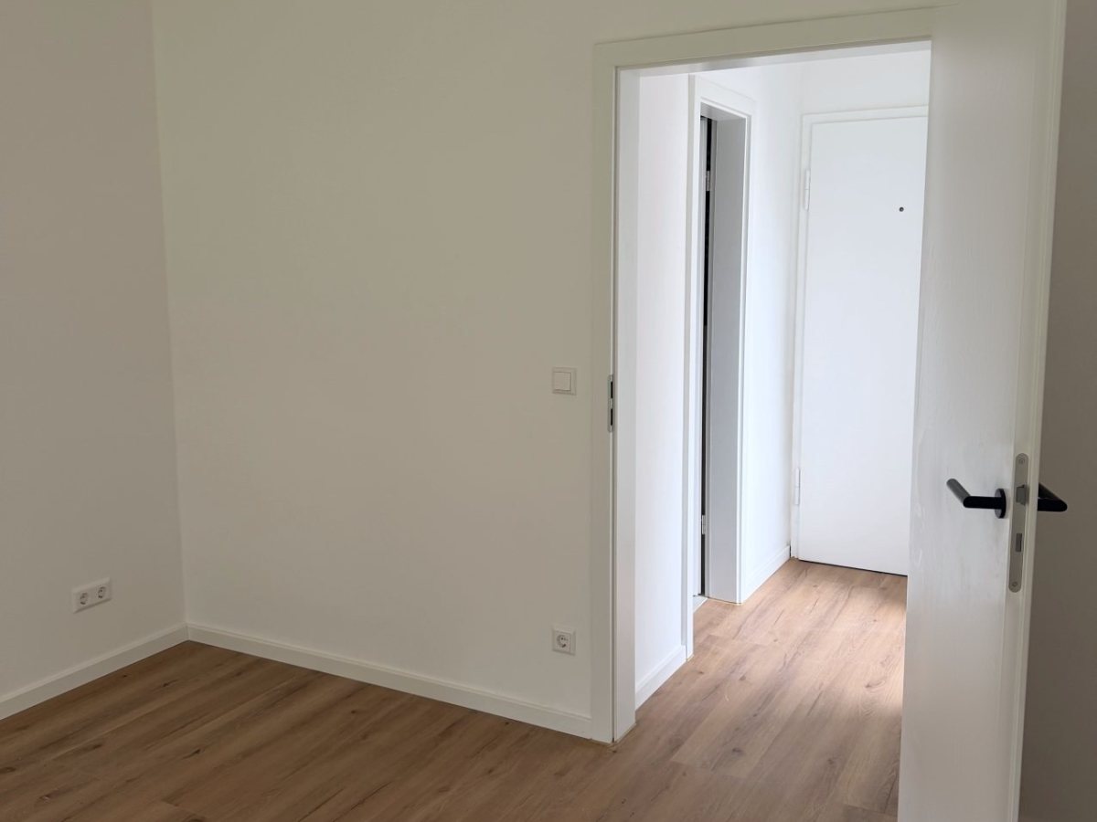 Sanierte Einzimmerwohnung: Raum mit neuer Innentür, Blick in den Flur und neuem Bodenbelag